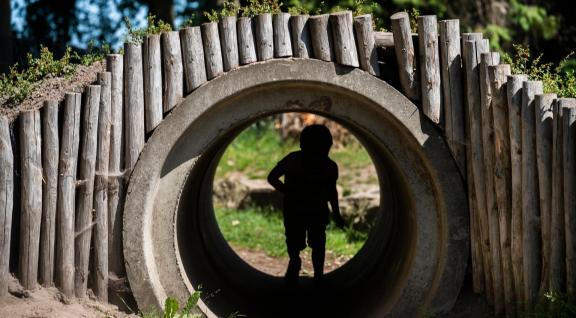 Kind speelt in tunnel of pijp in een speeltuin. Je ziet het kind in de schaduw ervan.