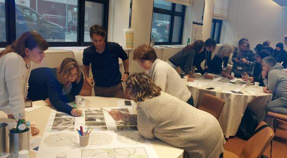 Three stables are lined up after one another, all surrounded by adults working together on paper during a stakeholder event.