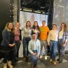 Six PhD students are lined up and smiling in front of the camera inside a university building